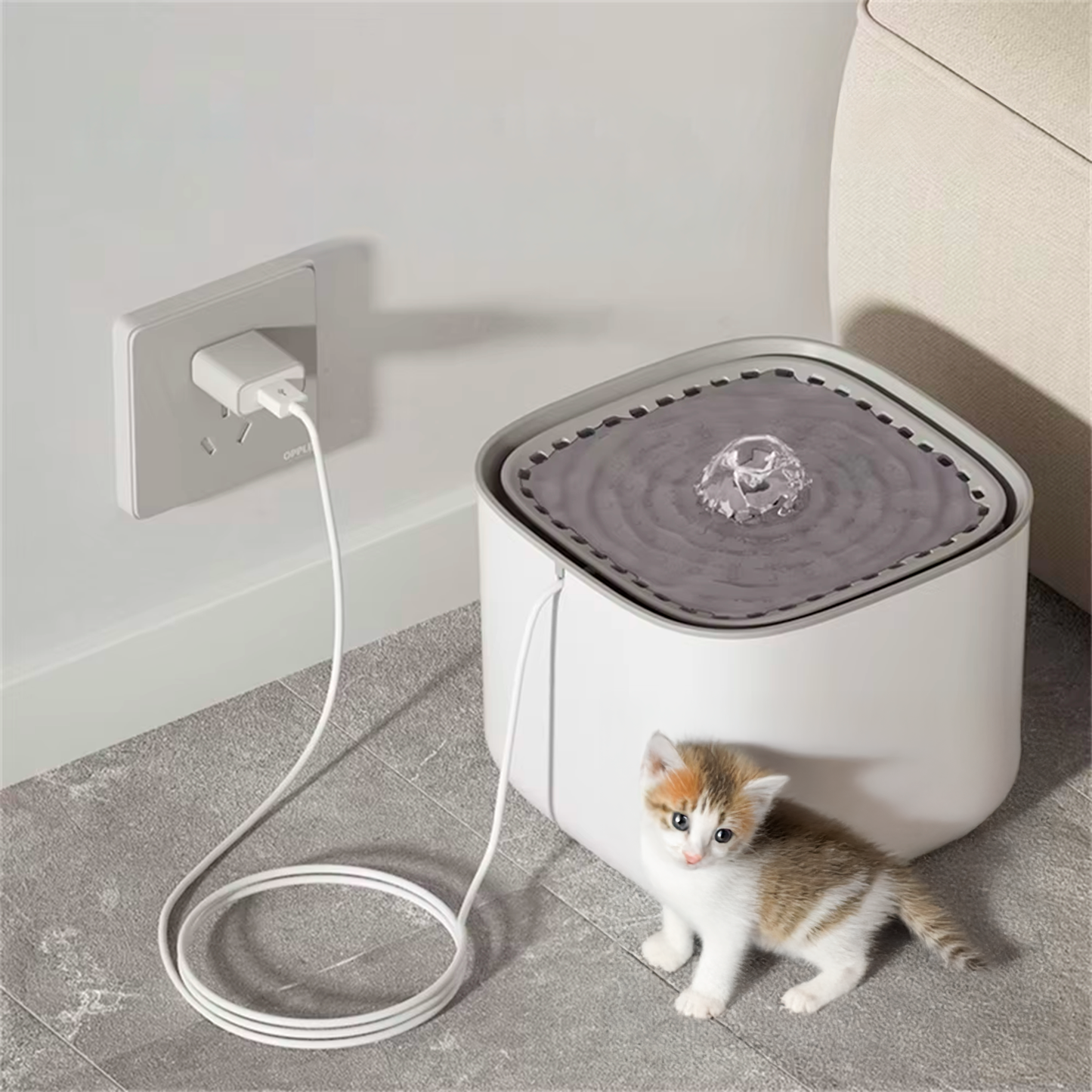Pet water fountain with kitten near it on a gray floor.