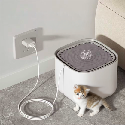 Pet water fountain with kitten near it on a gray floor.